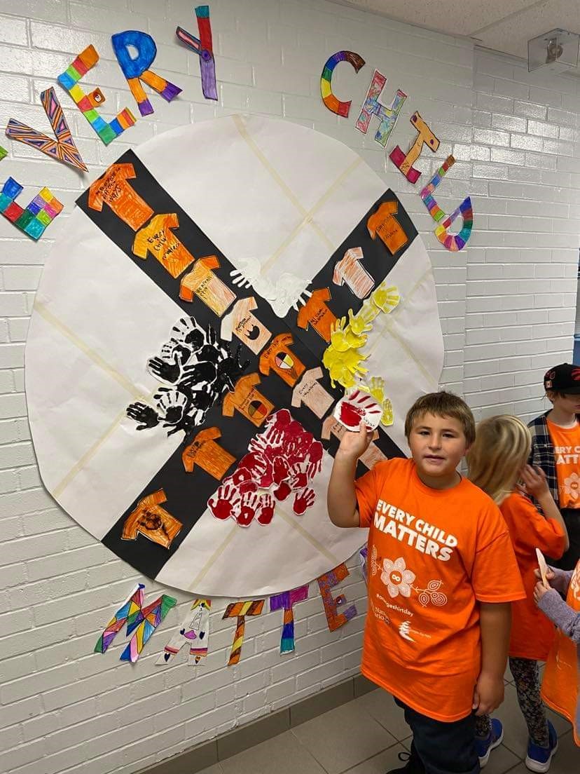 A young child poses in front of a 'Every Child Matters' mural.
