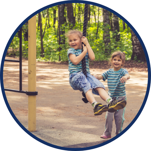 Two children wearing identical clothing. One is pushing the other on a rope swing.