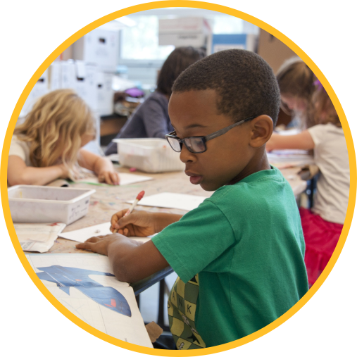 Young children drawing on papers while sitting a a long table.